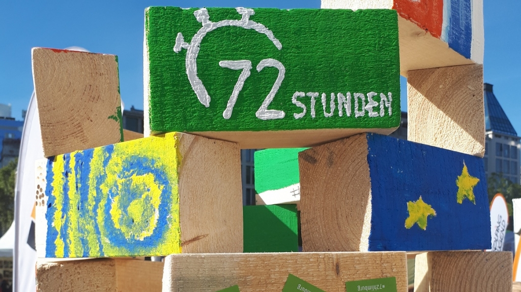Gestapelte und bemalte Holzbalken, u.a. mit dem Logo der 72 Stunden Aktion. Foto BDKJ Bundesstelle